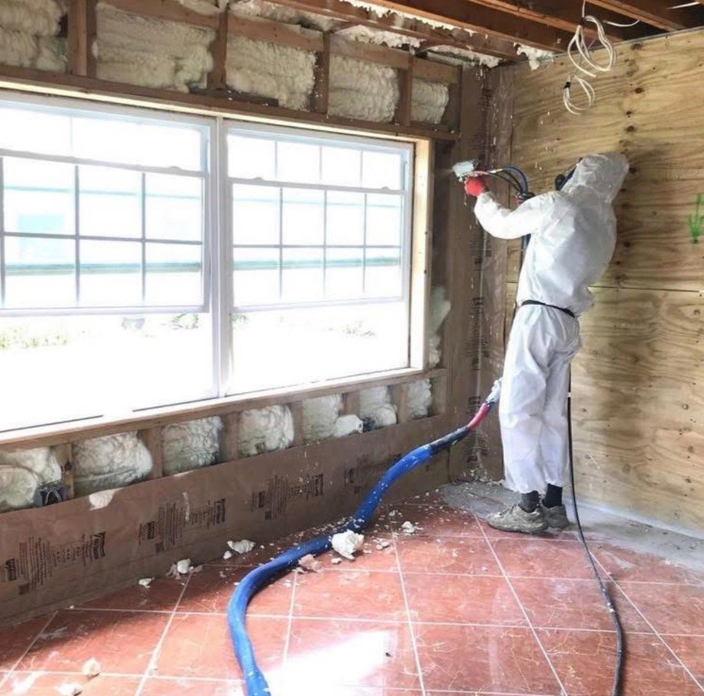 Installer in a protective suit spraying foam into a wall cavity